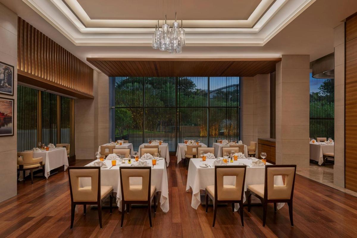 a restaurant with white tables and chairs and a chandelier at Bengaluru Marriott Hotel Whitefield in Bengaluru