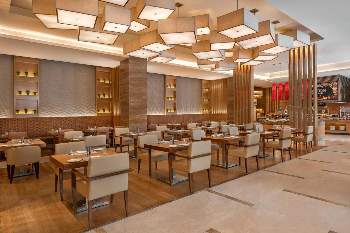 a restaurant with tables and chairs and a chandelier at Bengaluru Marriott Hotel Whitefield in Bengaluru