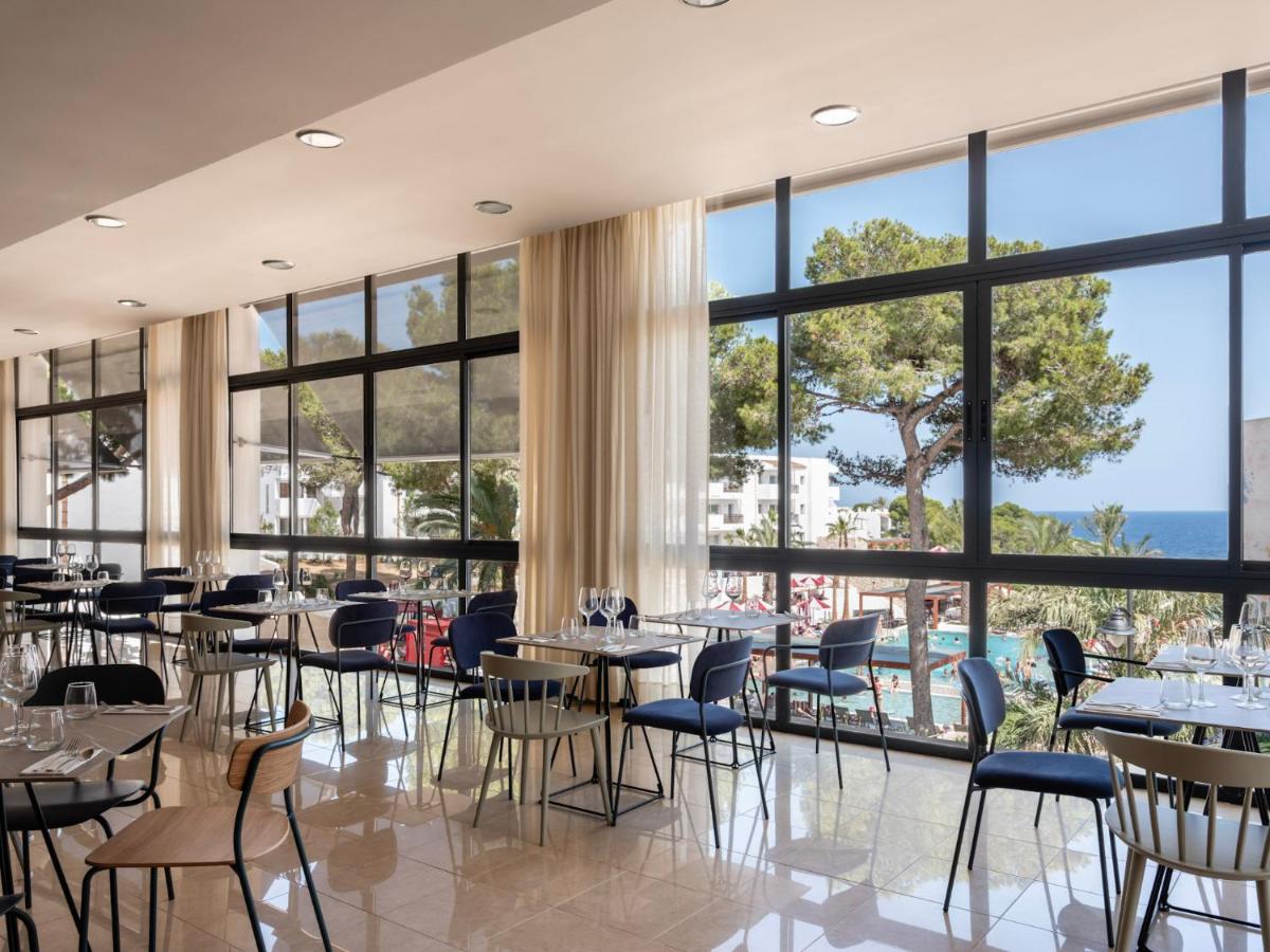 Un restaurante con mesas y sillas y grandes ventanales. en Inturotel Esmeralda Park, en Cala d´Or