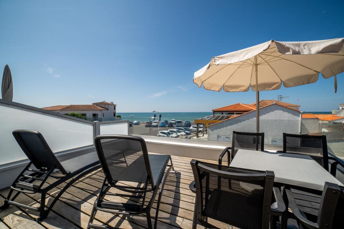 un patio avec une table, des chaises et un parasol dans l'établissement Hotel Les Dunes, à La Tranche-sur-Mer