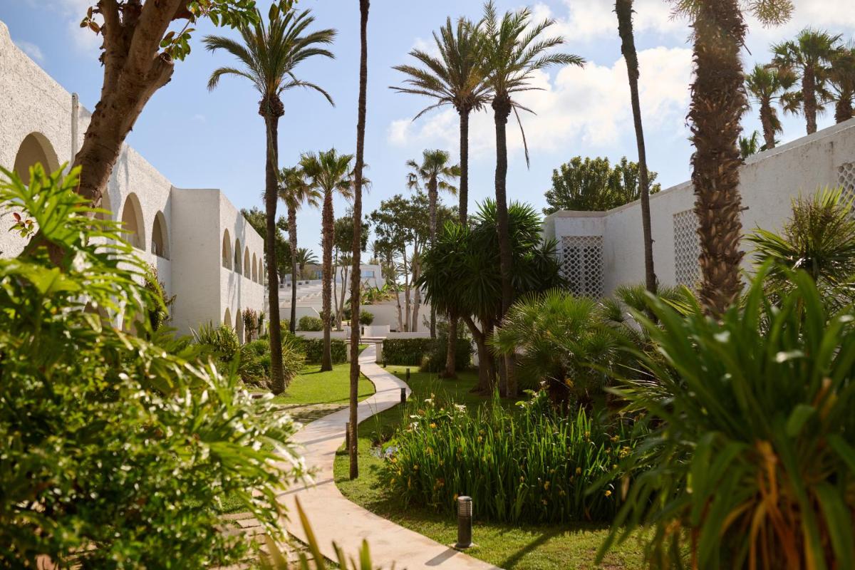 un jardín con palmeras y una acera en AluaSoul Menorca - Adults Only, en S'Algar