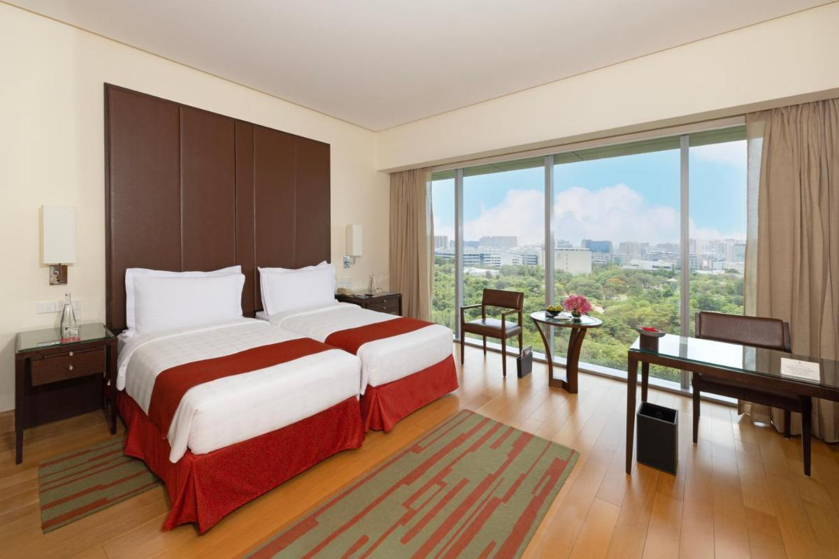 a bedroom with a bed and a desk and a large window at Trident Hyderabad in Hyderabad