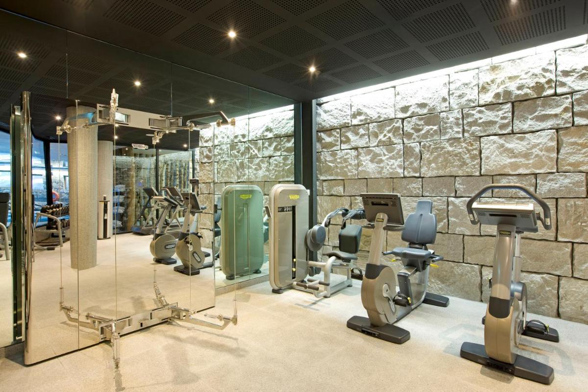 une salle de sport avec un mur en pierre et de nombreuses machines à bande de roulement dans l'établissement Altapura Hôtel & Spa Val Thorens, à Val Thorens