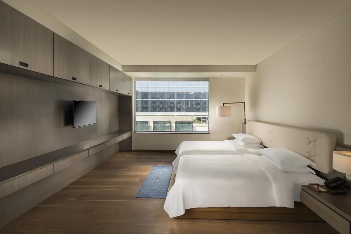 a bedroom with two beds and a large window at Andaz Delhi, by Hyatt in New Delhi a bedroom with two beds and a large window at Andaz Delhi, by Hyatt in New Delhi