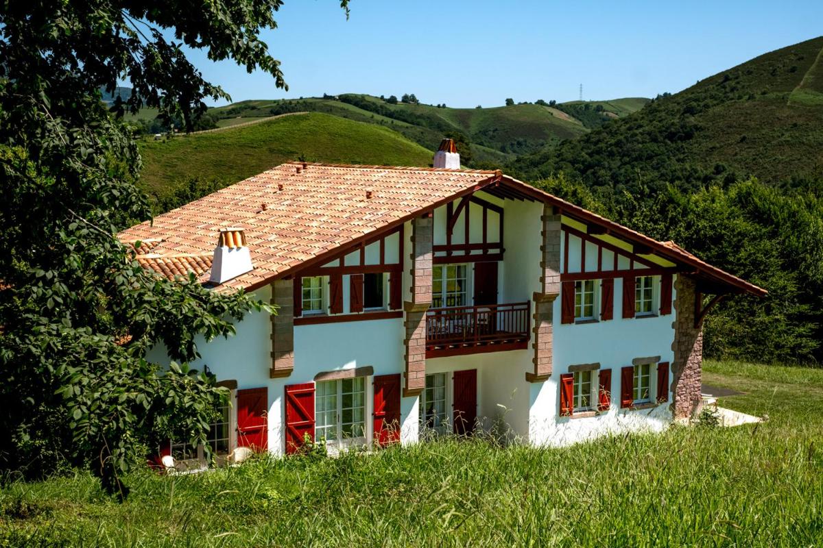 une maison blanche avec des fenêtres rouges et une colline dans l'établissement Auberge Ostapé, à Bidarray