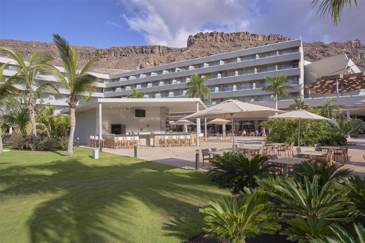Un hotel con mesas y sillas y una montaña al fondo. en Radisson Blu Resort & Spa, Gran Canaria Mogan, en Puerto de Mogán
