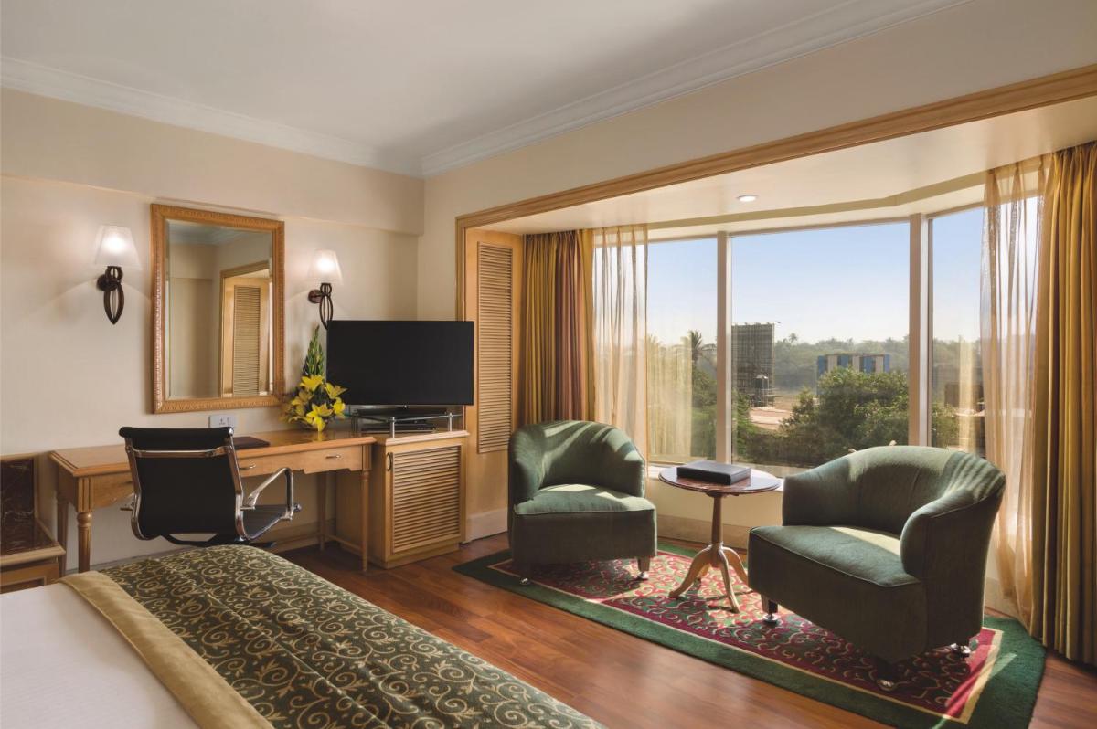 a hotel room with a bed and a desk and chairs at Ramada Plaza By Wyndham Palm Grove in Mumbai