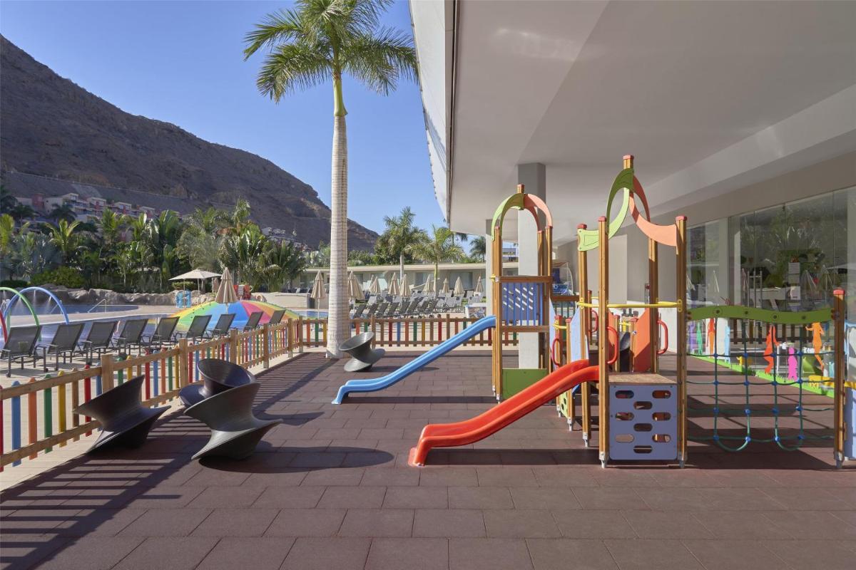 Un parque infantil en un complejo turístico con una palmera. en Radisson Blu Resort & Spa, Gran Canaria Mogan, en Puerto de Mogán