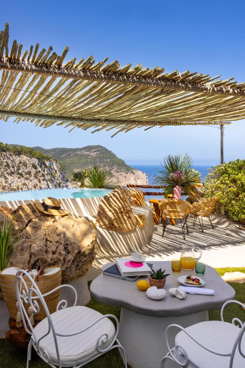 Un patio con mesa y sillas y el mar. en Hacienda Na Xamena, Ibiza, en Na Xamena