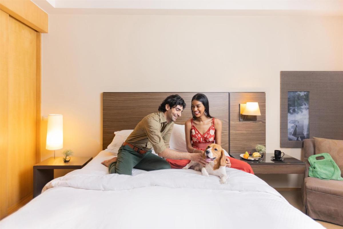 two people sitting on a bed with a dog at Grand Hyatt Mumbai Hotel and Residences in Mumbai