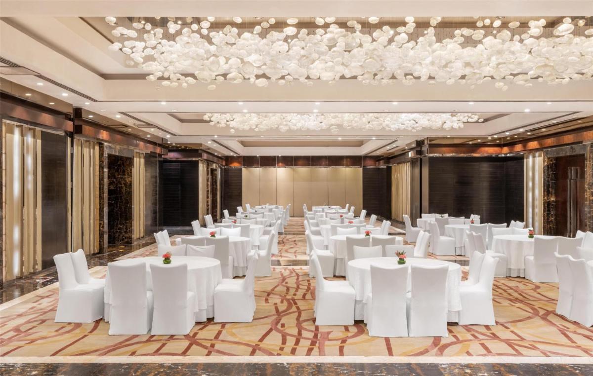 a ballroom with white tables and chairs and a chandelier at Radisson Blu Plaza Delhi Airport in New Delhi a ballroom with white tables and chairs and a chandelier at Radisson Blu Plaza Delhi Airport in New Delhi
