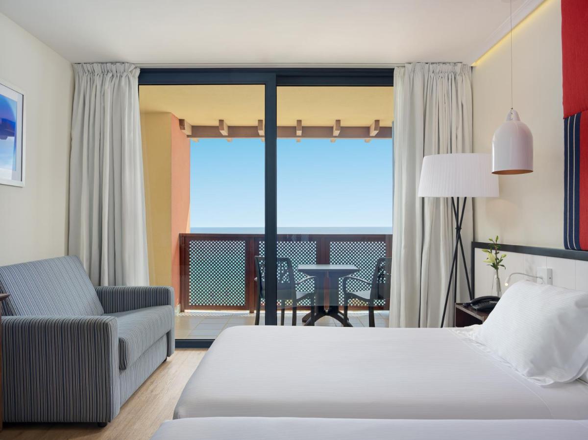 1 dormitorio con 1 cama, 1 silla y balcón en H10 Tindaya, en Costa Calma