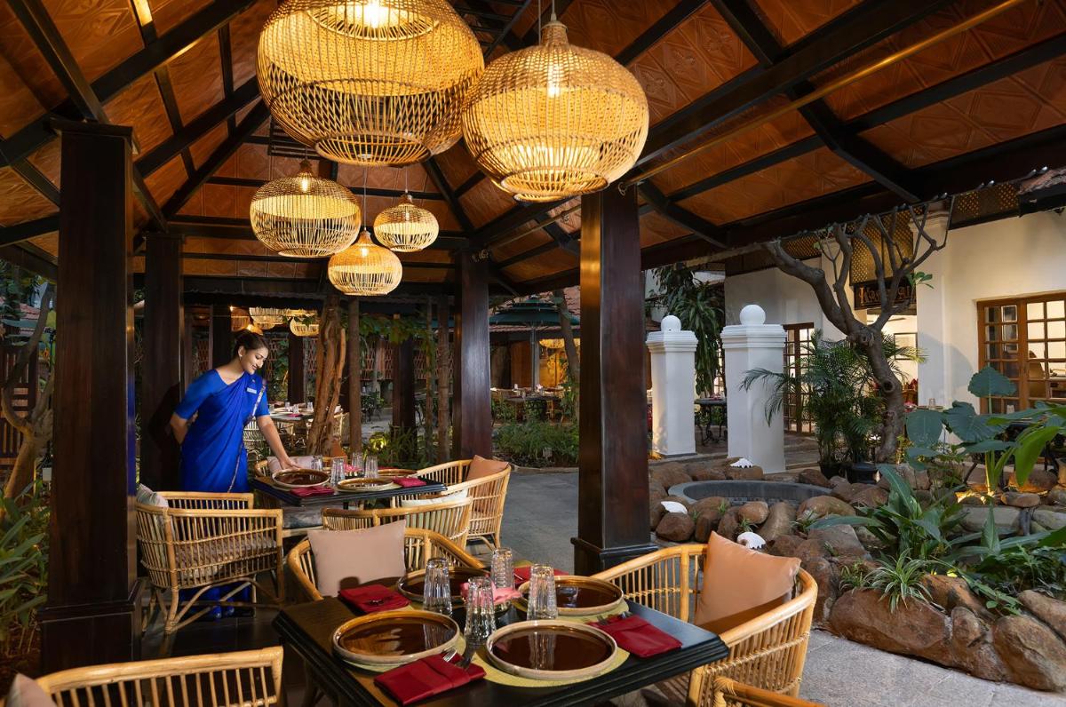 a man standing in a restaurant with tables and chandeliers at Vivanta Bengaluru Residency Road in Bengaluru a man standing in a restaurant with tables and chandeliers at Vivanta Bengaluru Residency Road in Bengaluru
