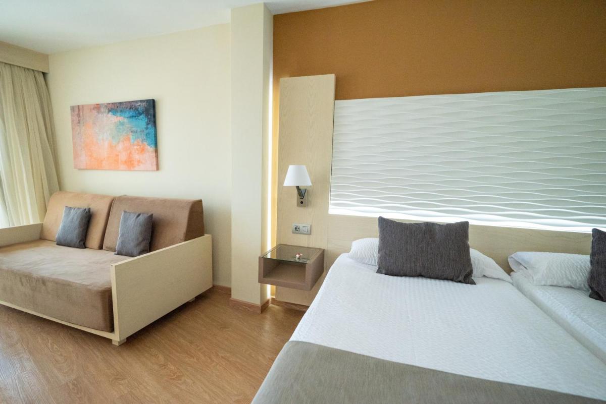 una habitación de hotel con dos camas y una silla en HL Suite Nardos - Only Adults, en Maspalomas