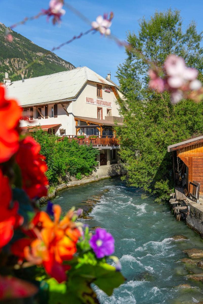 une rivière avec des fleurs devant un bâtiment dans l'établissement Logis Hôtel et Spa Le Christiania, à La Salle Les Alpes