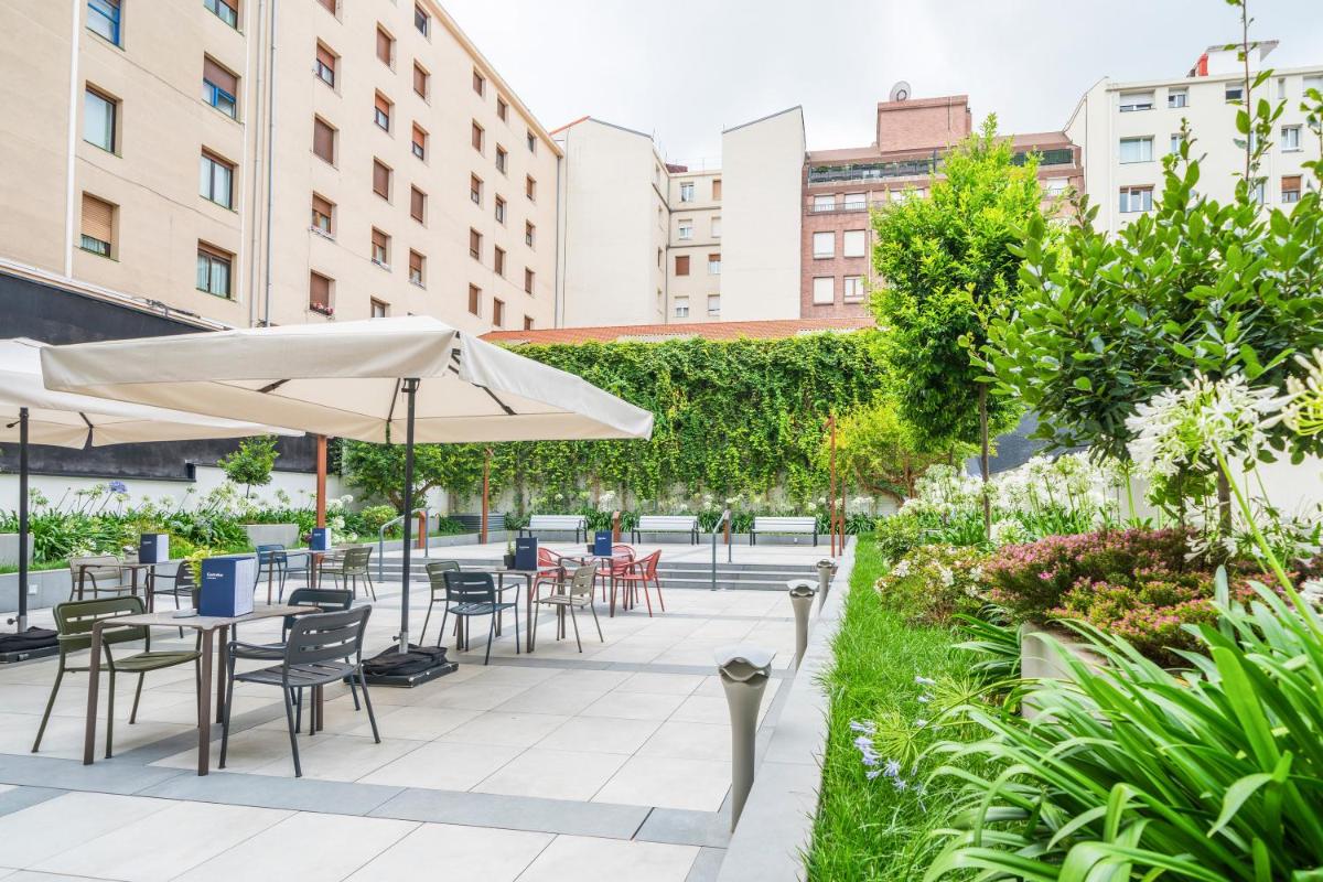 Un patio al aire libre con mesas, sillas y sombrillas. en Catalonia Gran Vía Bilbao, en Bilbao