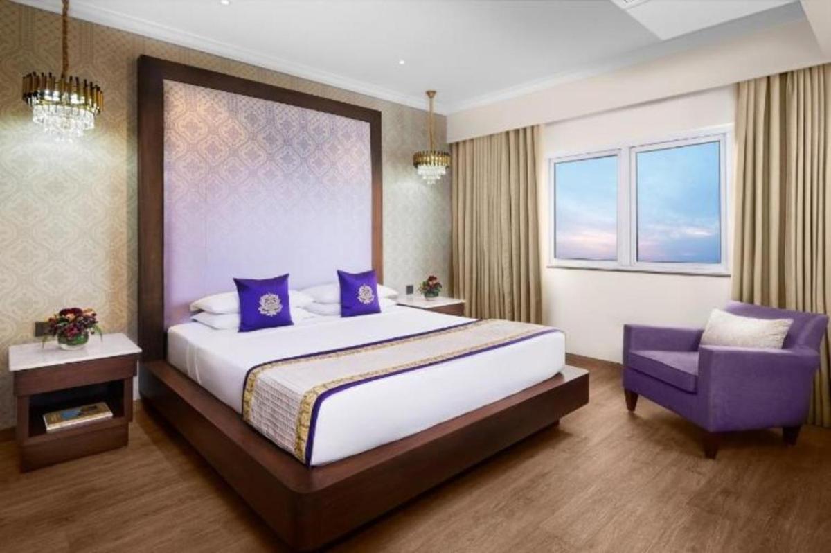 a bedroom with a large bed and a purple chair at Vivanta Bengaluru Residency Road in Bengaluru a bedroom with a large bed and a purple chair at Vivanta Bengaluru Residency Road in Bengaluru