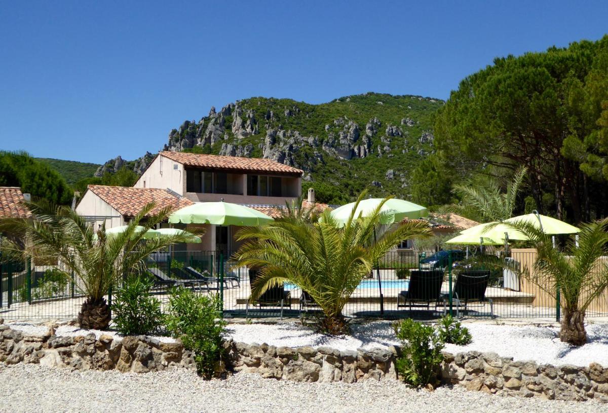 un complexe avec une piscine avec des parasols verts et des palmiers dans l'établissement Auberge Val Moureze Hôtel & Spa, à Mourèze