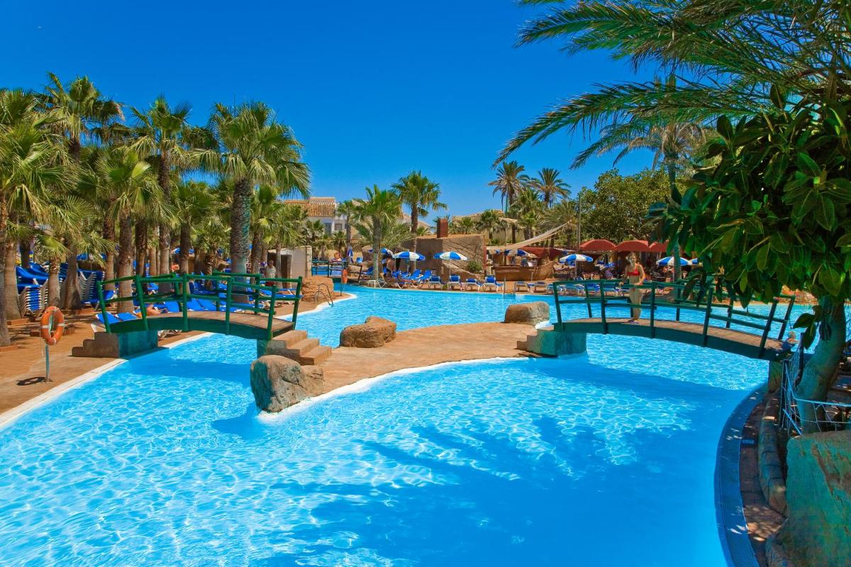 una piscina en un complejo con agua azul y palmeras en Playalinda, en Roquetas de Mar