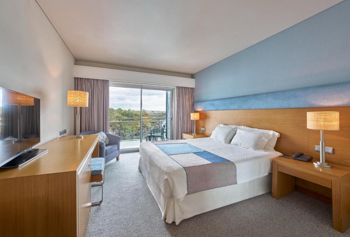 um quarto de hotel com uma cama, uma escrivaninha e uma televisão em Hotel Do Caracol em Angra do Heroísmo