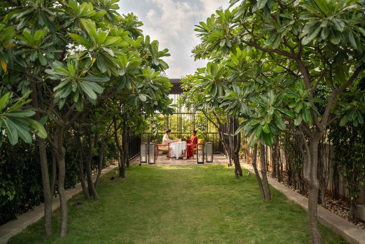 two people sitting at a table in a garden with trees at Four Seasons Hotel Bengaluru at Embassy ONE in Bengaluru two people sitting at a table in a garden with trees at Four Seasons Hotel Bengaluru at Embassy ONE in Bengaluru