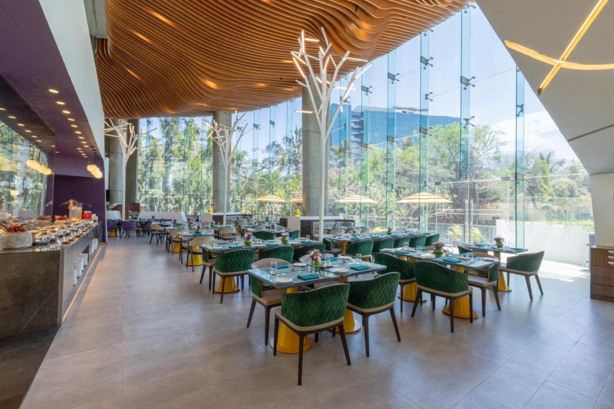a dining room with tables and chairs and large windows at Vivanta Bengaluru, Whitefield in Bengaluru