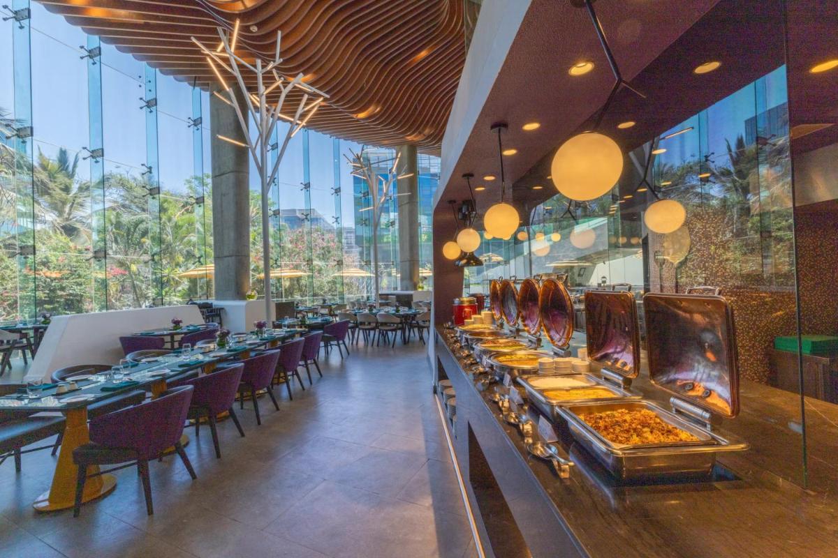 a restaurant with long tables and chairs and windows at Vivanta Bengaluru, Whitefield in Bengaluru