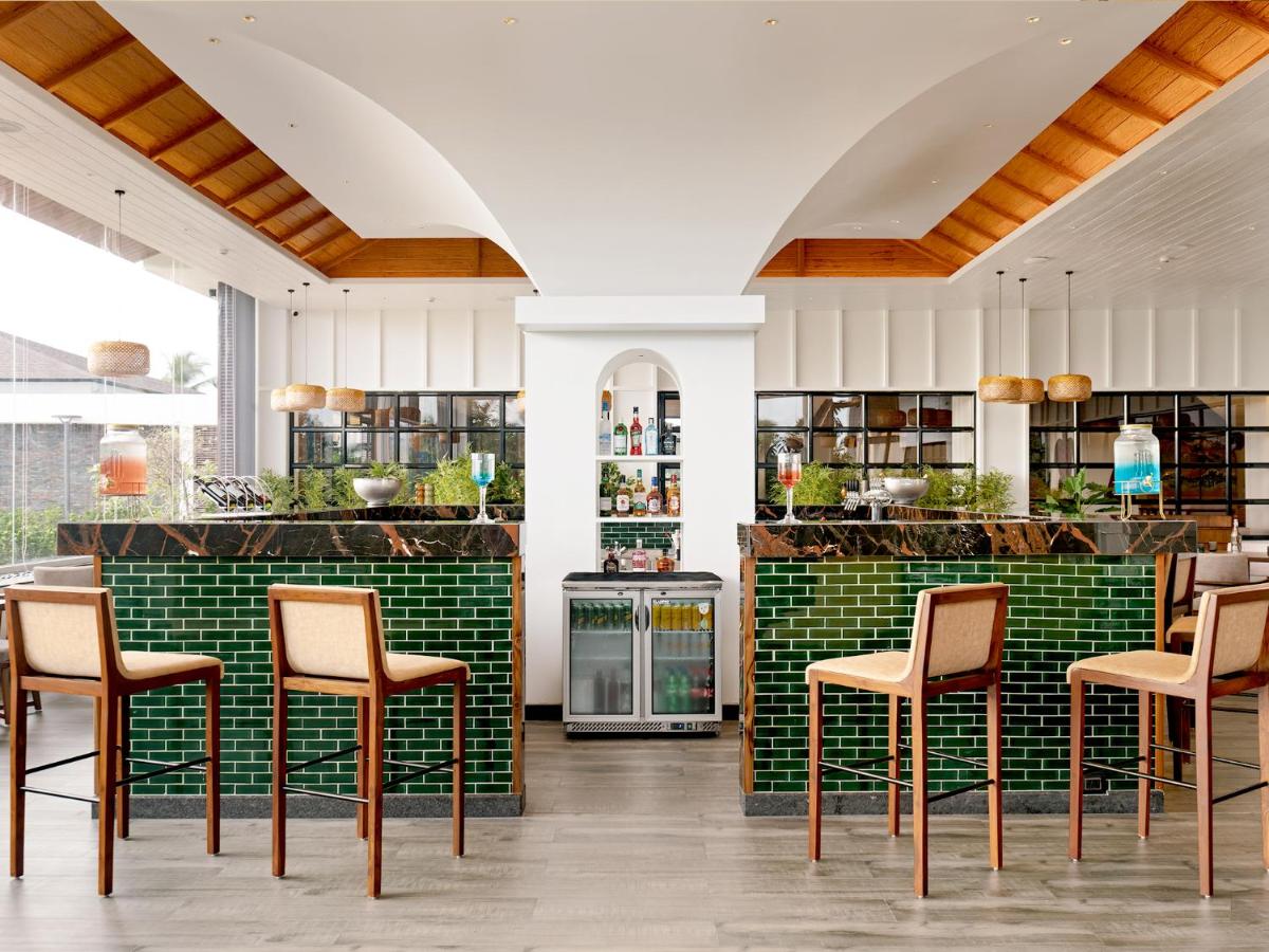a kitchen with a bar with chairs and green tiles at Gateway Goa, Palolem in Palolem