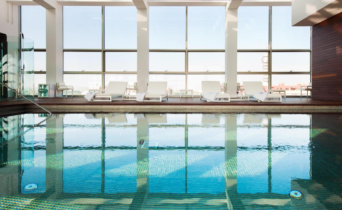 Una piscina con tumbonas blancas en un edificio. en Hotel Reina Petronila, en Zaragoza