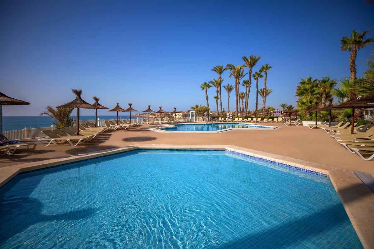 Una piscina en un resort con palmeras y el océano. en Hotel Servigroup La Zenia 4 Sup, en Playas de Orihuela
