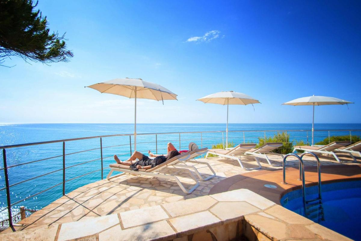 Una piscina con sillas y sombrillas y el océano. en Hotel Servigroup Montíboli, en Villajoyosa