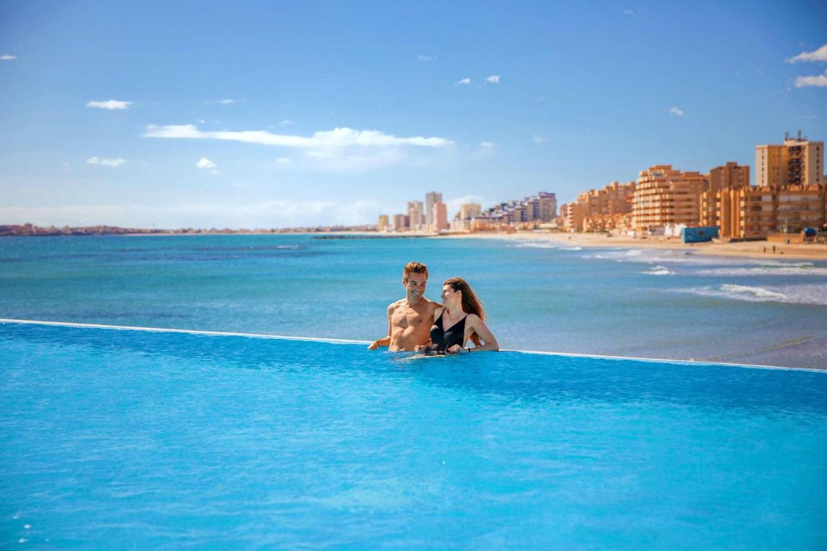 Un hombre y una mujer sentados en una piscina infinita en la playa. en Hotel Servigroup Galua, en La Manga del Mar Menor
