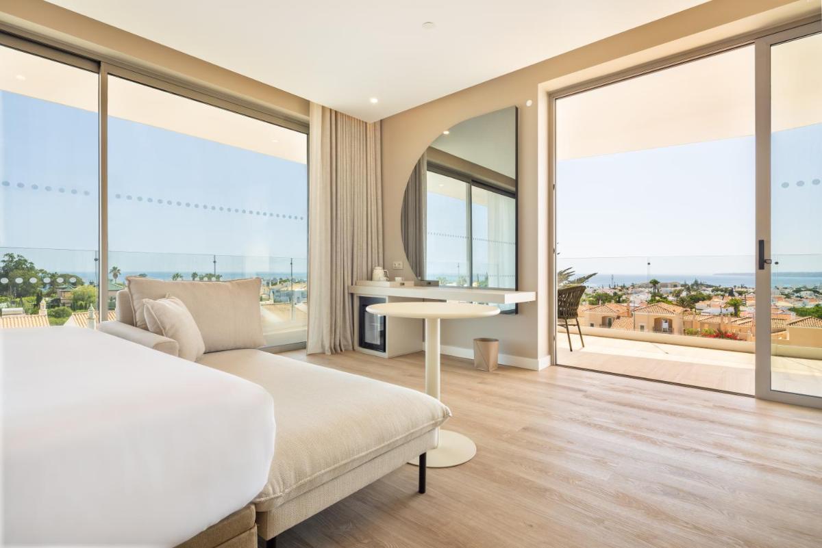 um quarto com uma cama e uma mesa e janelas grandes em Castelo Suites Hotel em Albufeira