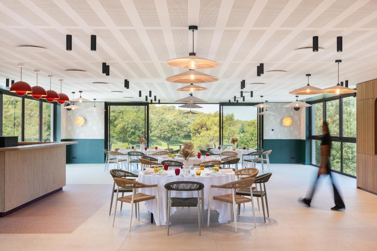 une salle à manger avec des tables et des chaises blanches et des fenêtres dans l'établissement Mercure Brignoles Golf de Barbaroux & Spa, à Brignoles