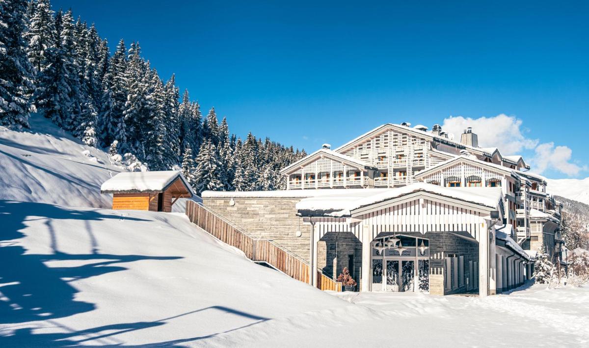 un grand bâtiment dans la neige avec des arbres enneigés dans l'établissement Ecrin Blanc Resort Courchevel - Aquapark, à Courchevel
