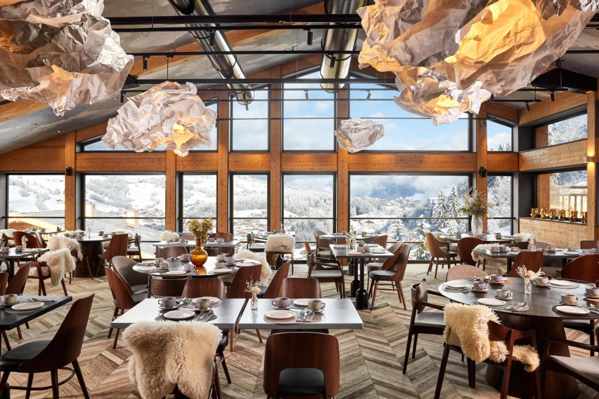 un restaurant avec des tables et des chaises et de grandes fenêtres dans l'établissement Hôtel L'Arboisie, à Megève