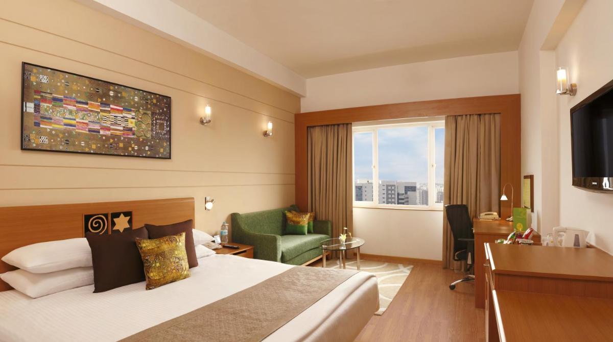 a hotel room with a bed and a desk and a window at Lemon Tree Premier Hitec City Hyderabad in Hyderabad