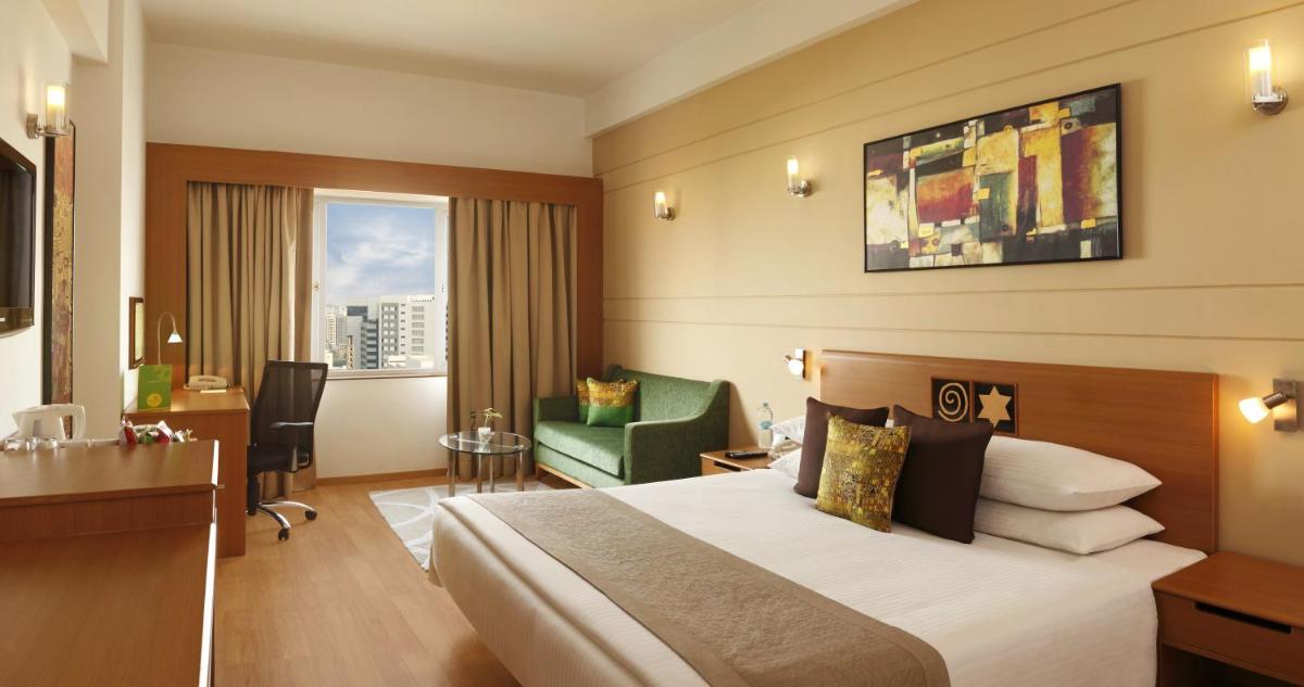 a hotel room with a bed and a green chair at Lemon Tree Premier Hitec City Hyderabad in Hyderabad a hotel room with a bed and a green chair at Lemon Tree Premier Hitec City Hyderabad in Hyderabad