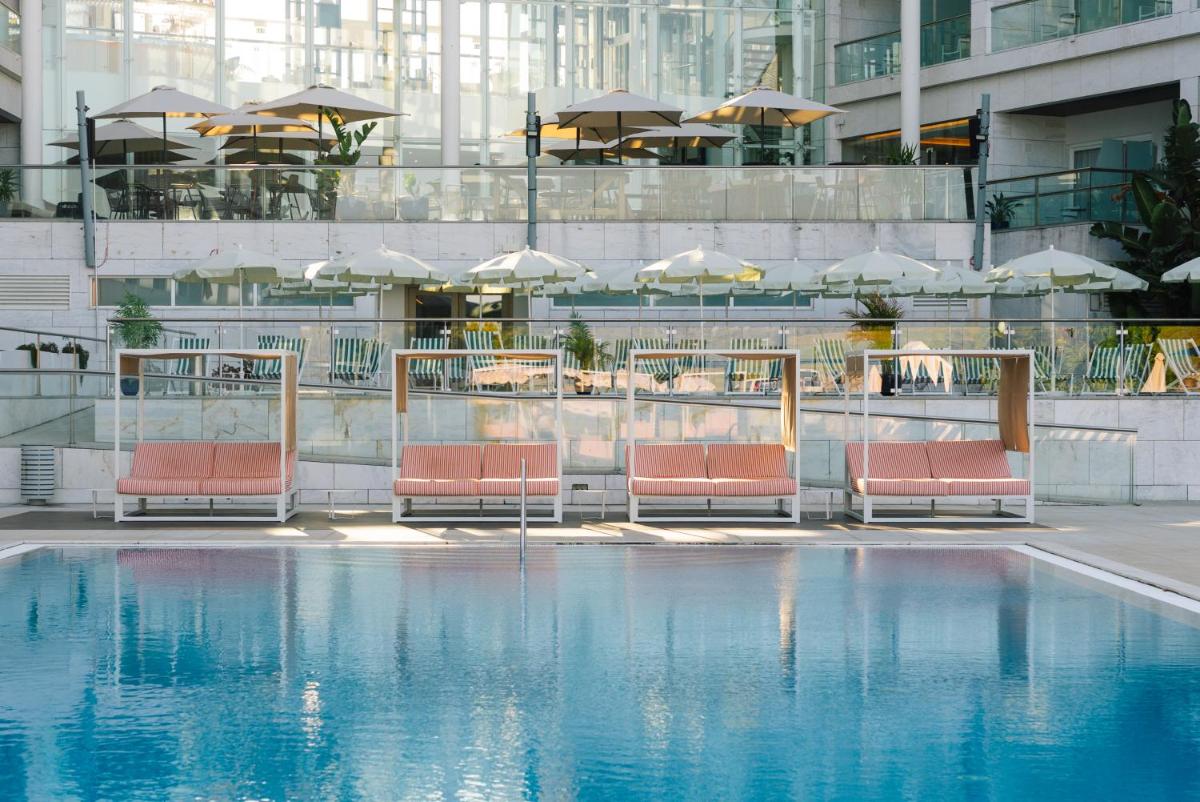 uma piscina com cadeiras e guarda-sóis em um prédio em Crowne Plaza - Caparica Lisbon em Costa da Caparica