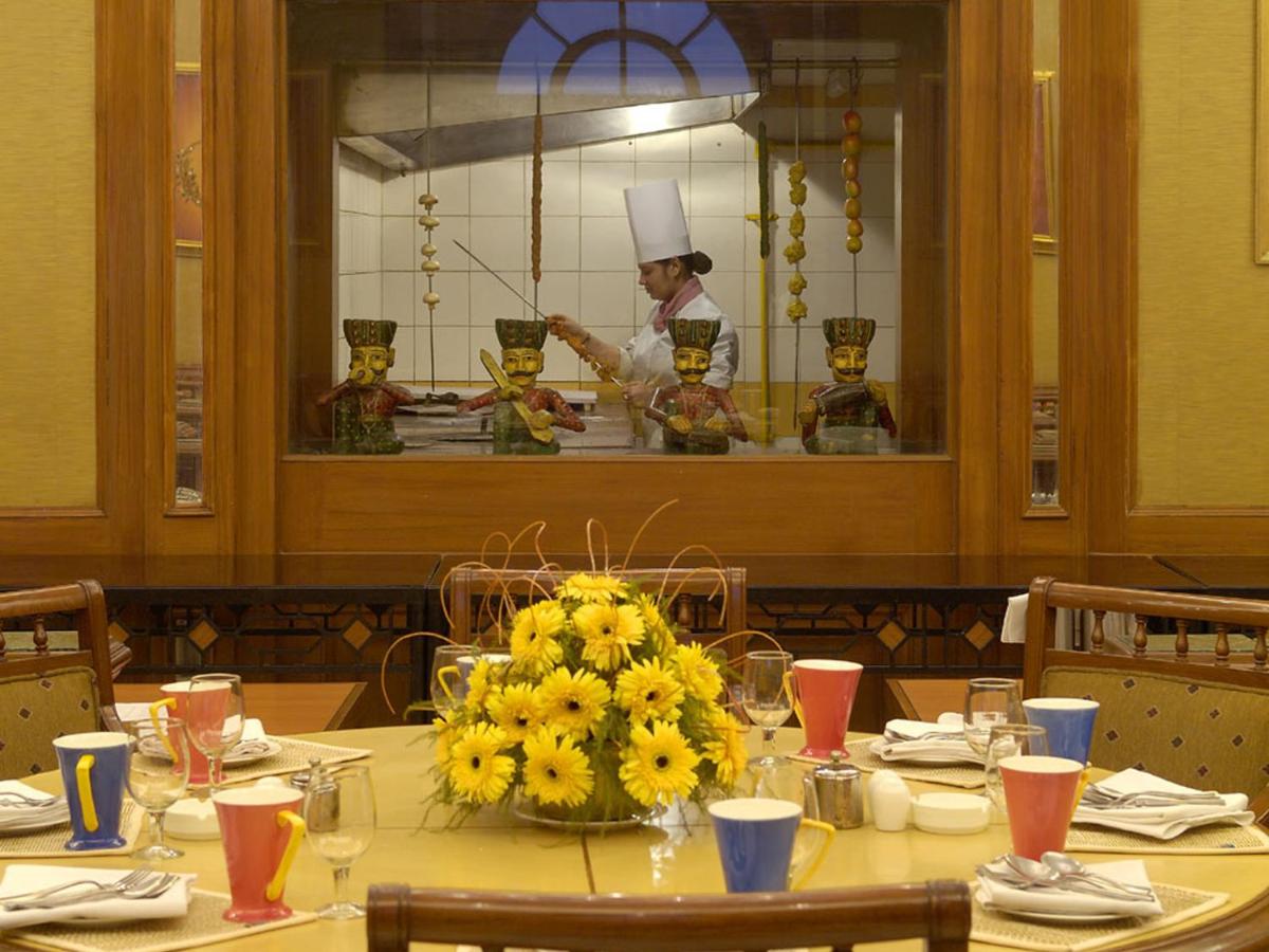 a table with yellow flowers and a chef in the kitchen at The Lalit Laxmi Vilas Palace in Udaipur