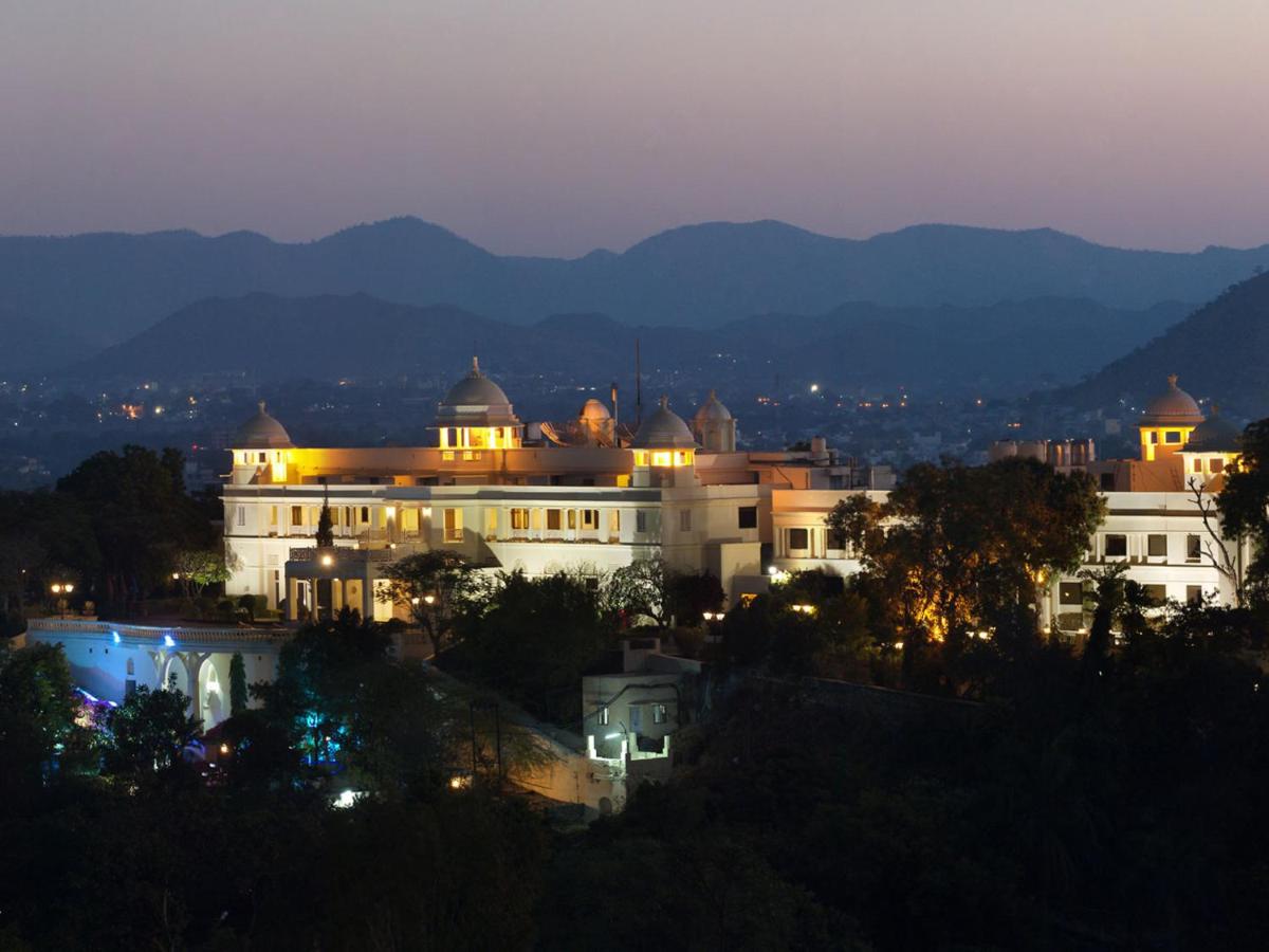 a large white building at night with mountains in the background at The Lalit Laxmi Vilas Palace in Udaipur