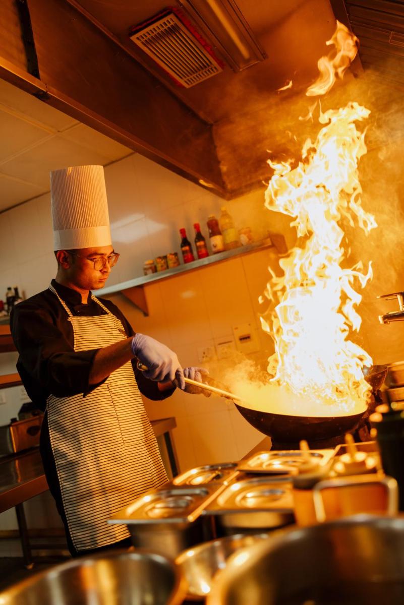 a man cooking in a wok in a kitchen at Sunday Hotel Chandigarh Zirakpur in Zirakpur