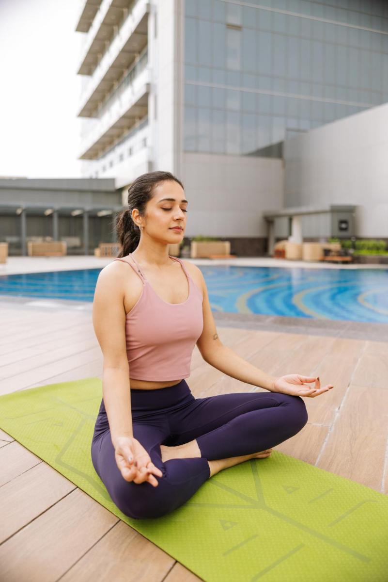a woman sitting in a yoga pose in front of a pool at Sunday Hotel Chandigarh Zirakpur in Zirakpur