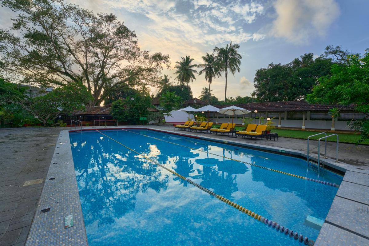 a large blue swimming pool with chairs and trees at Casino Hotel - CGH Earth, Cochin in Cochin