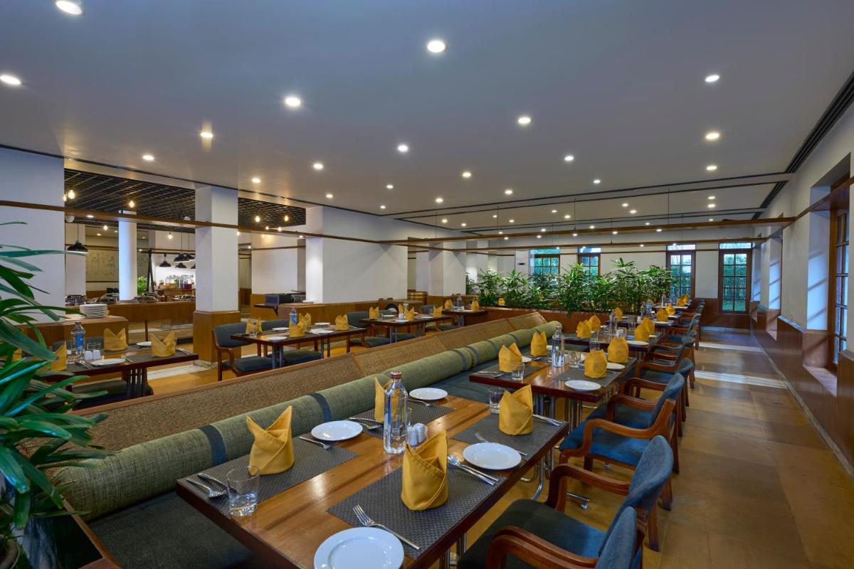 a restaurant with wooden tables and chairs and a long couch at Casino Hotel - CGH Earth, Cochin in Cochin