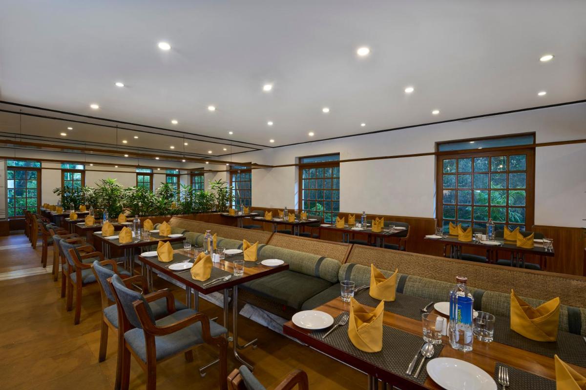 a restaurant with long tables and chairs and windows at Casino Hotel - CGH Earth, Cochin in Cochin