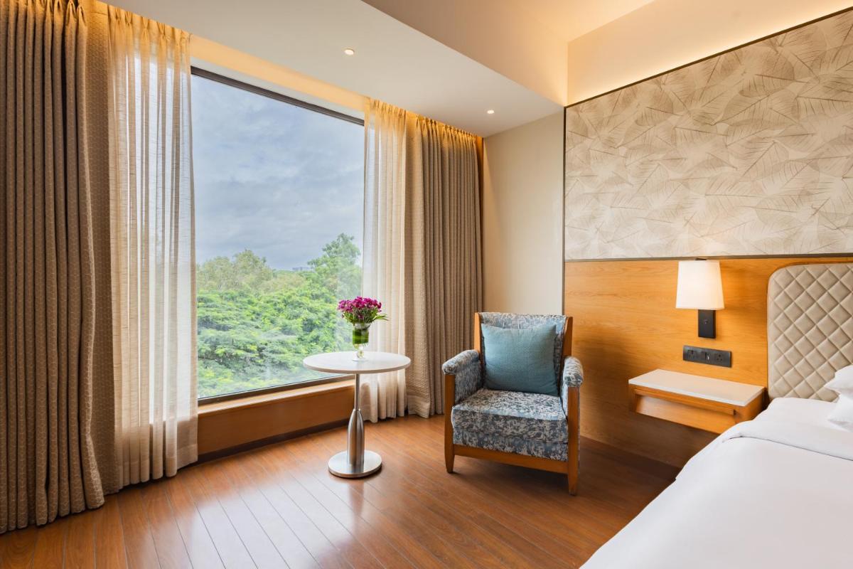 a hotel room with a bed and a chair and a window at Hyatt Pune in Pune