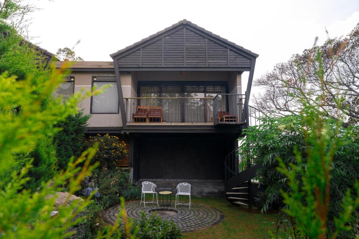 a house with a balcony with two chairs in the yard at WelcomHeritage Ayatana Ooty in Ooty