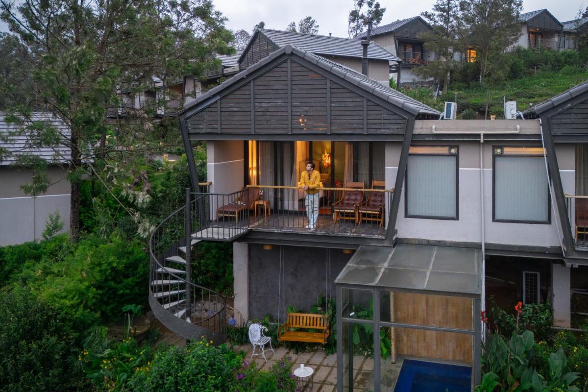 a man standing on the balcony of a house at WelcomHeritage Ayatana Ooty in Ooty