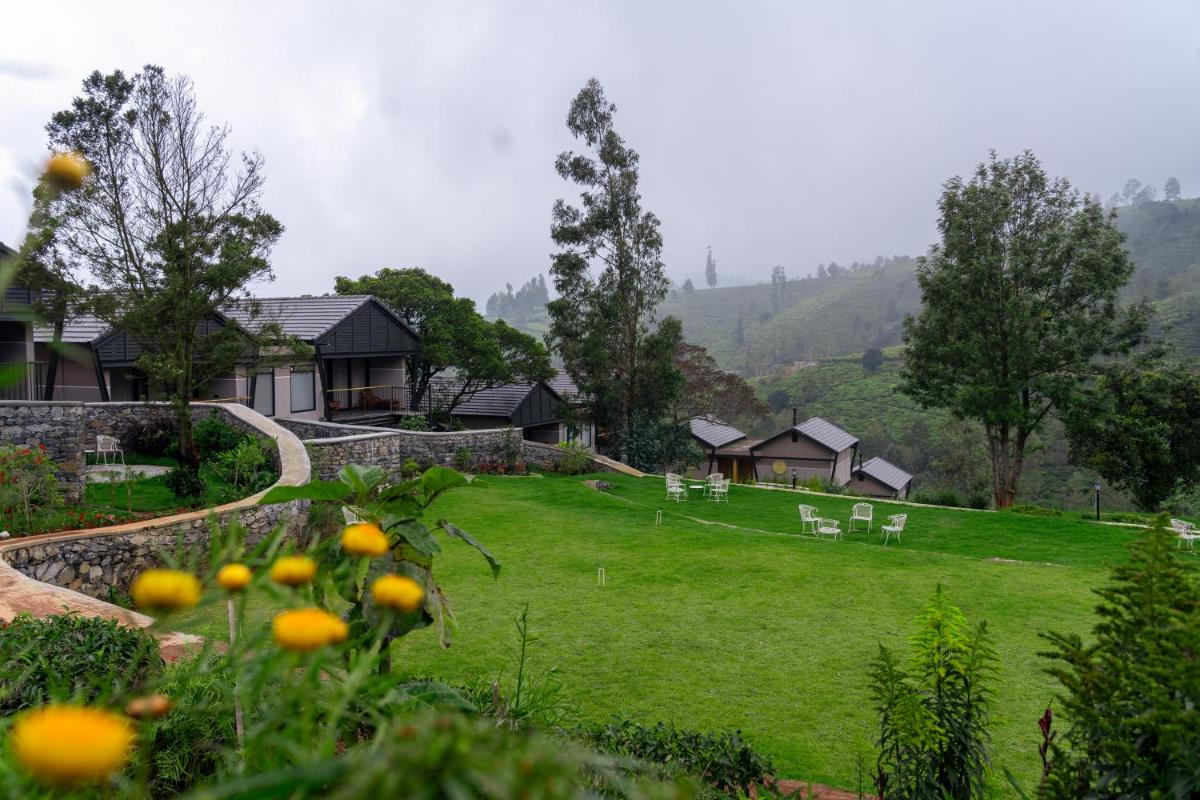 a green yard with white chairs and a house at WelcomHeritage Ayatana Ooty in Ooty